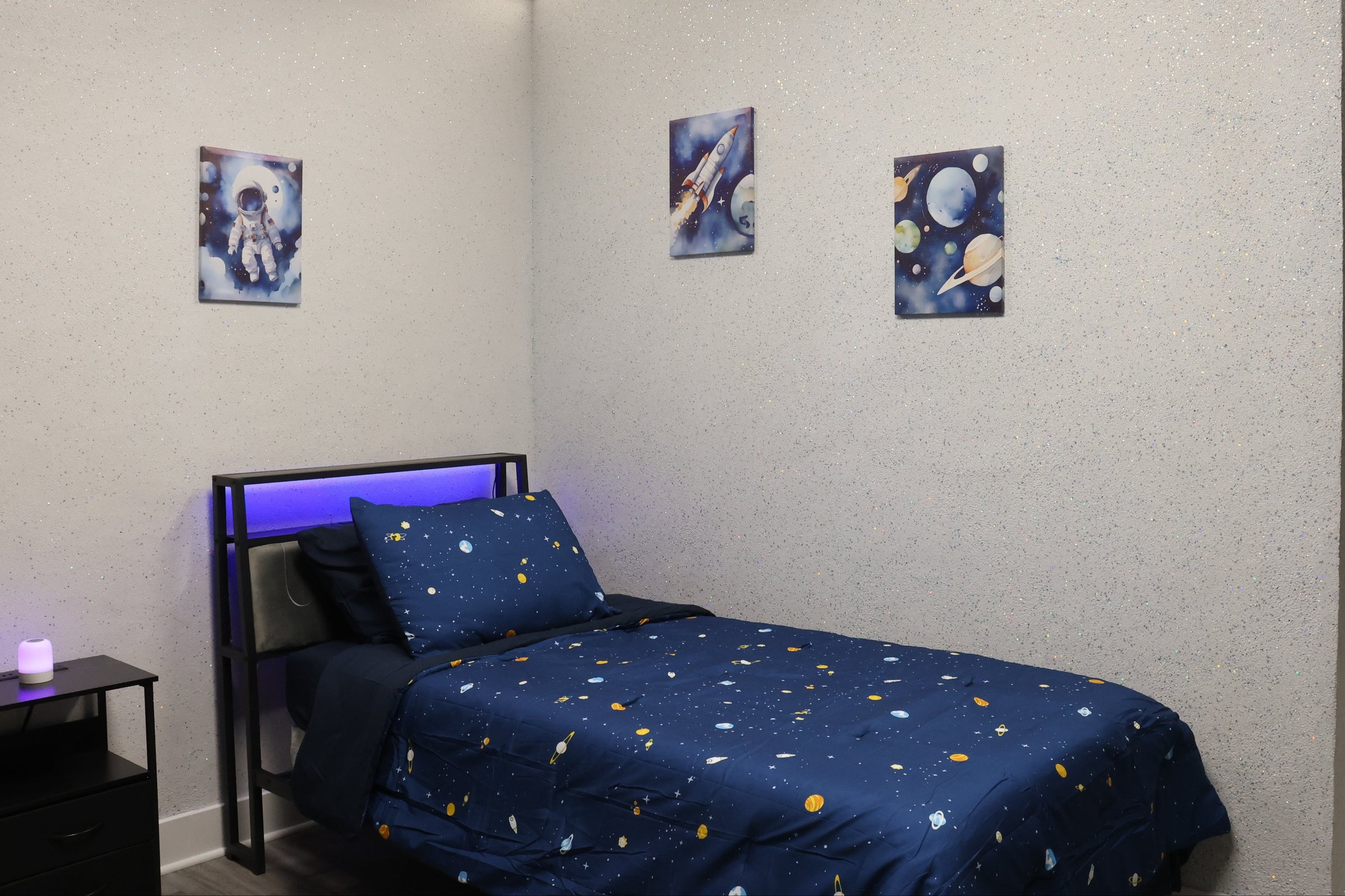 Bedroom with a bed featuring a space-themed bedding set, nightstands, and wall art.